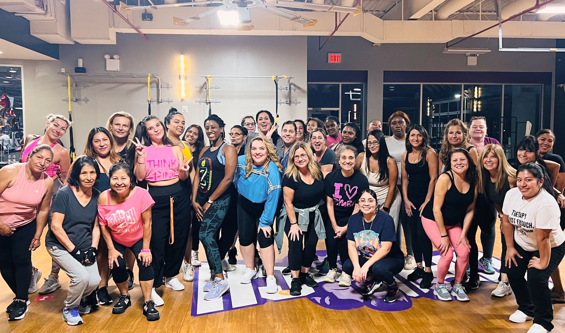 Large group photo of people standing inside a gym, all smiling to the camera.