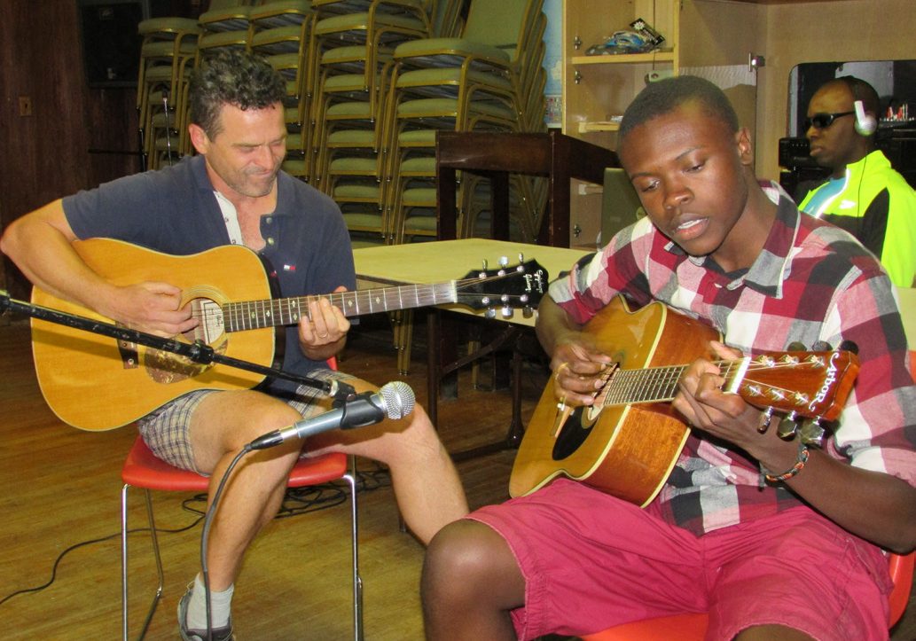 two guys strumming acoustic guitars in empty gymnasium