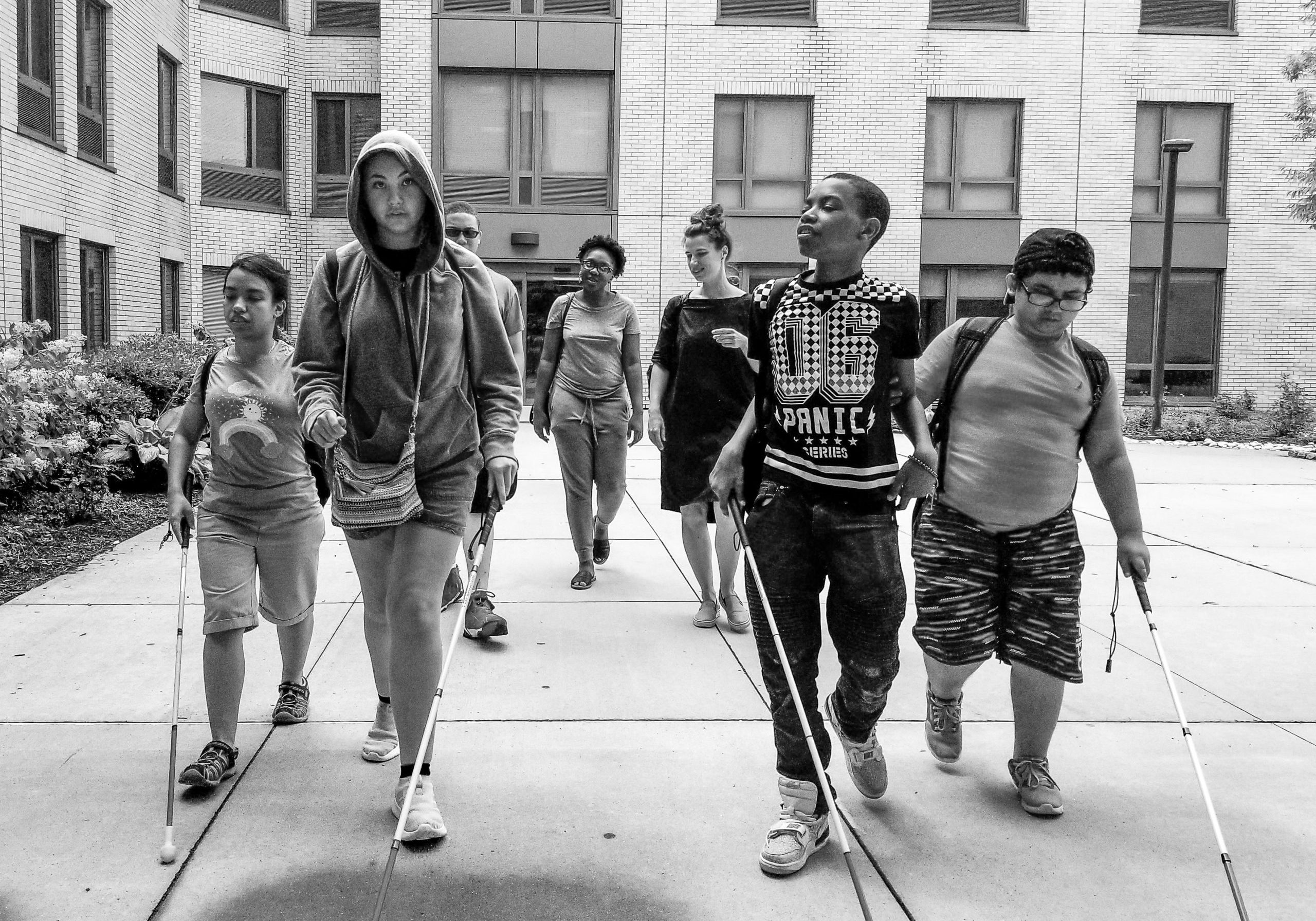 Black and white photo of a group of confident young adults with canes, walking toward the camera.