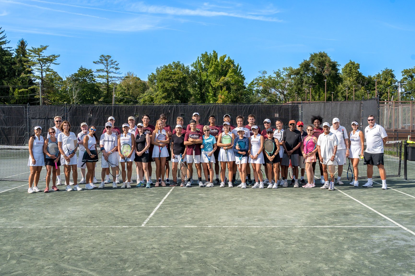 Large group photo of tennis players standing in front of the net, all smiling to the camera.