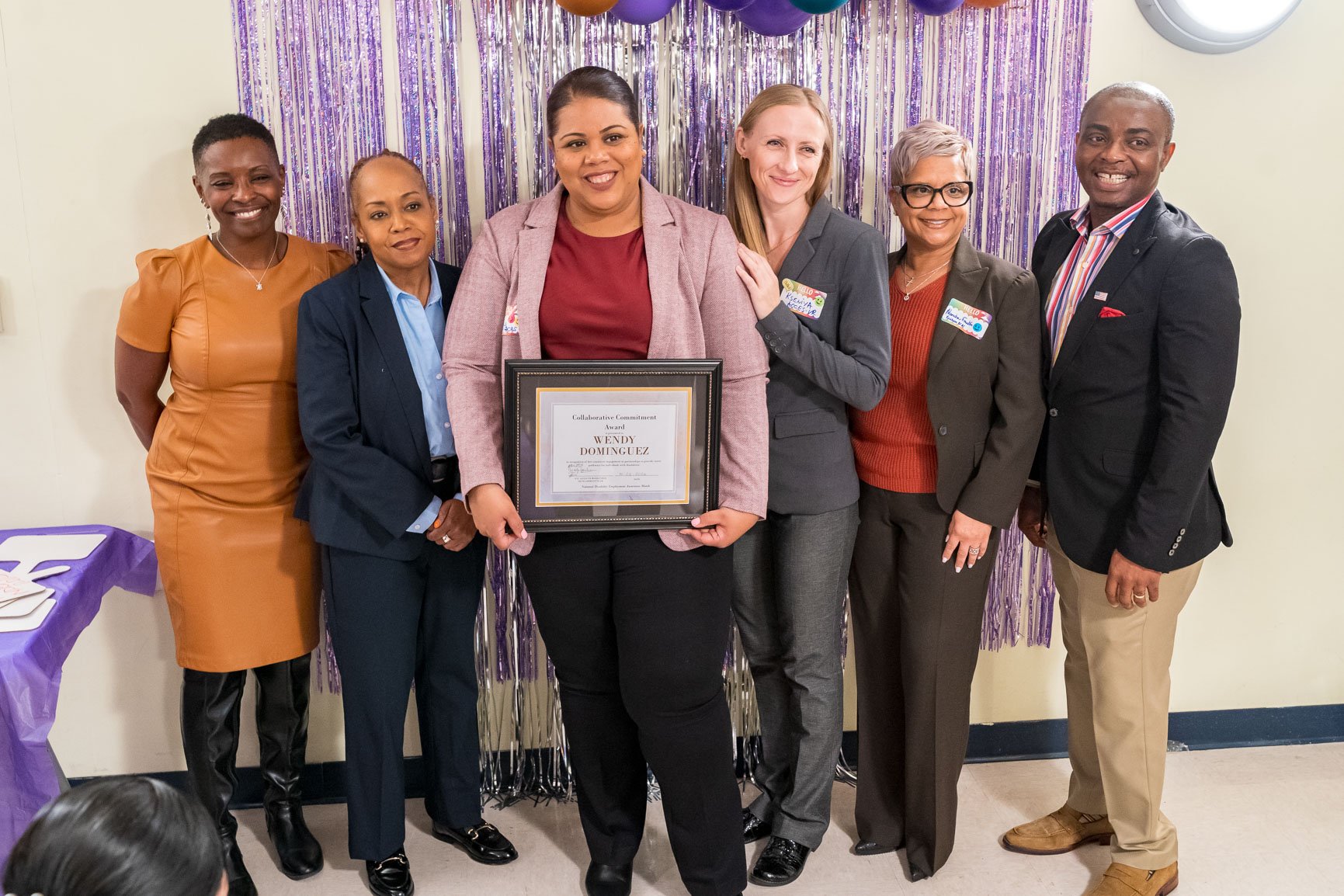 Group photo of ACCES-VR staff standing together and smiling, as one of their members holds a framed award.