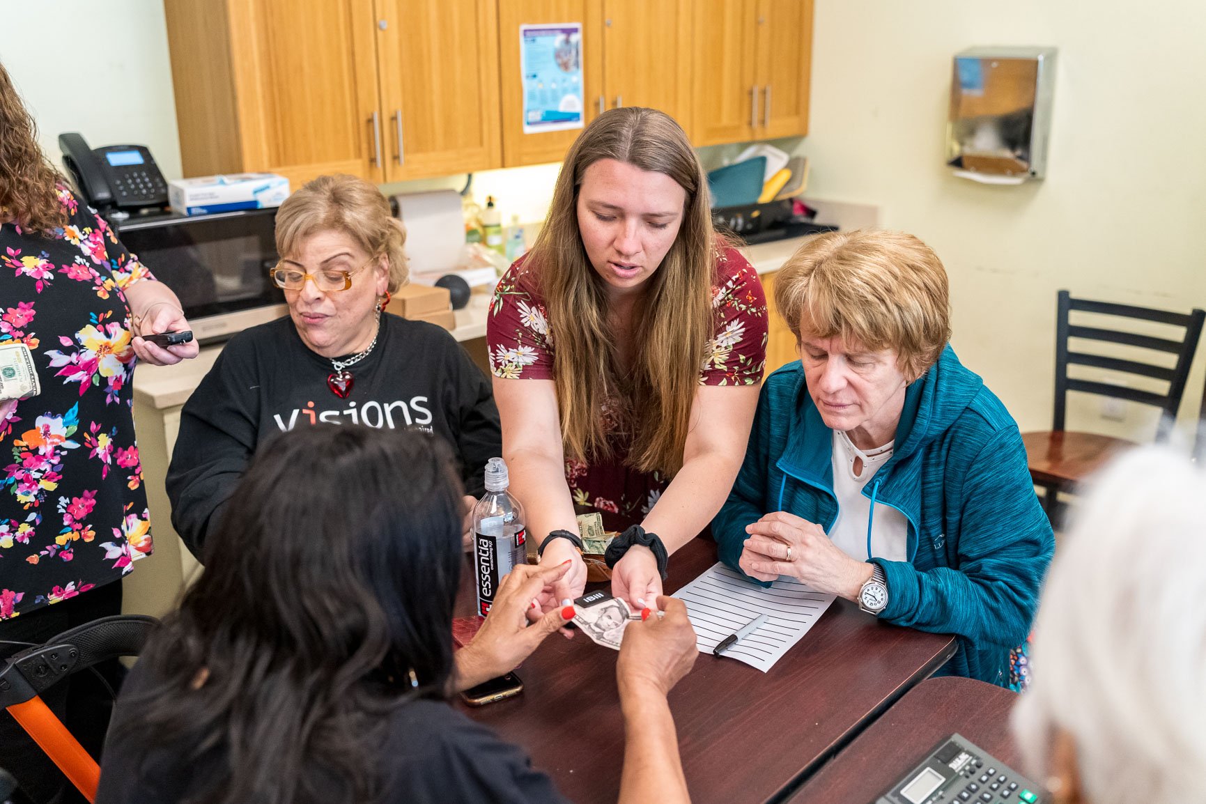 Photo of a Vision Rehabilitation Therapist (center) introducing a group of three participants to a handheld money identifier.