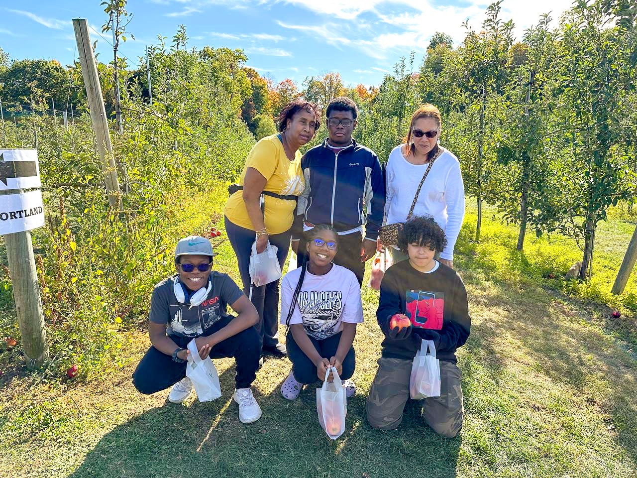 Group photo of six people standing in an apple orchard smiling to the camera
